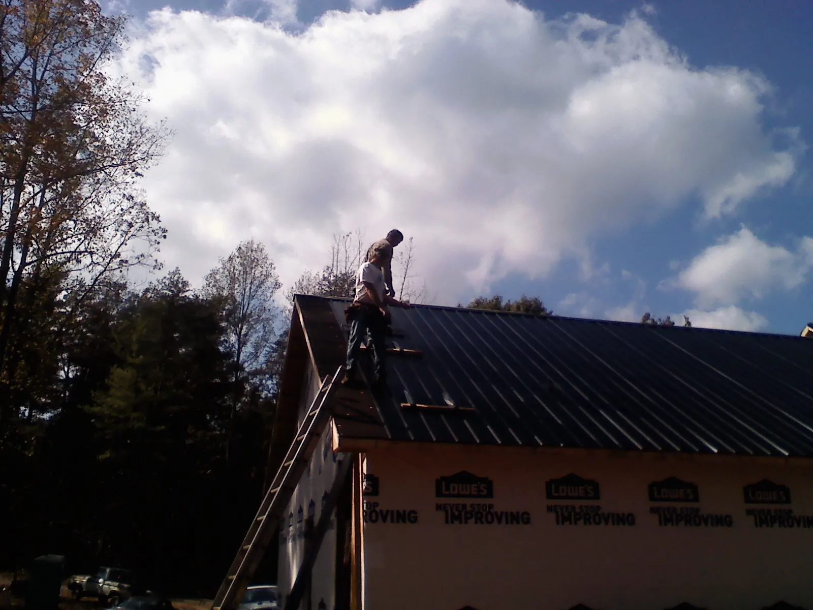 Roofer fastening dark metal panels high against a cloudy sky, from a Roof Inspection job in Rosalia